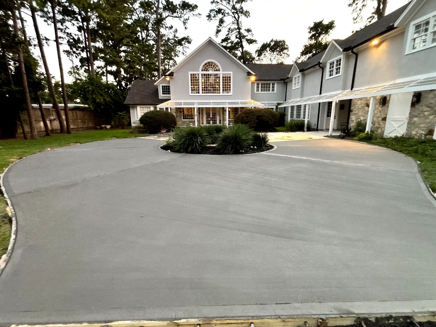 The same property with its finished concrete driveway sweeping around a planted island at dusk