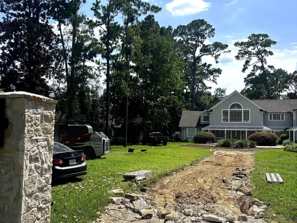 Old driveway demolished to rubble and dirt in front of a two-story home, before base preparation