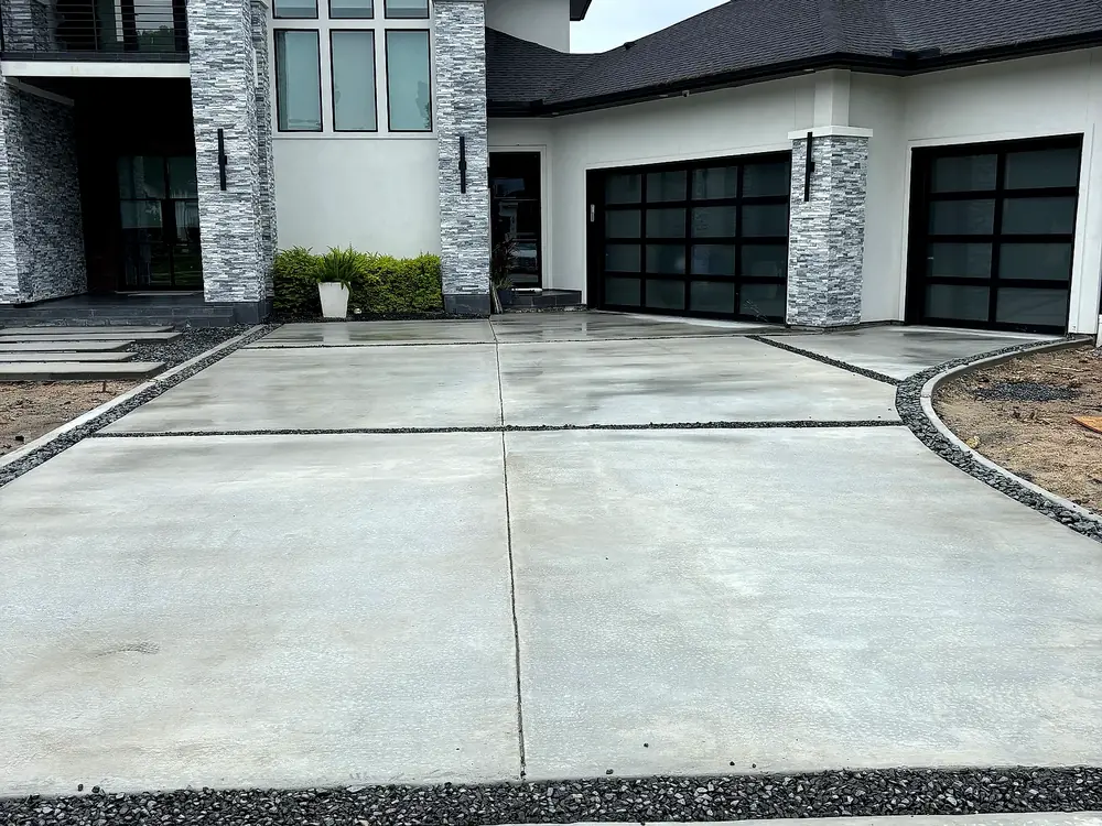 Fresh gray concrete driveway with dark rock borders at a modern new-construction home