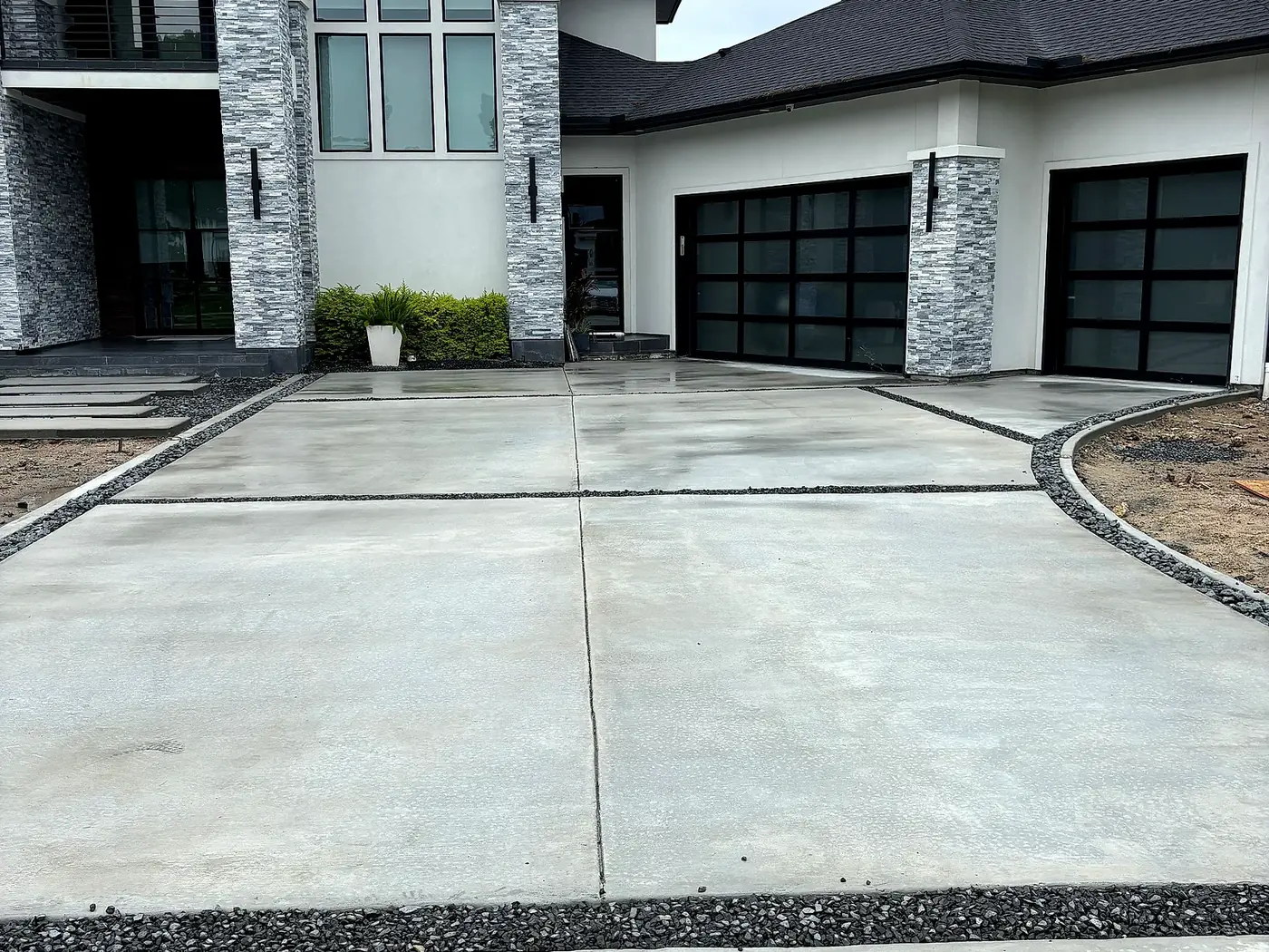 Fresh gray concrete driveway with dark rock borders at a modern new-construction home