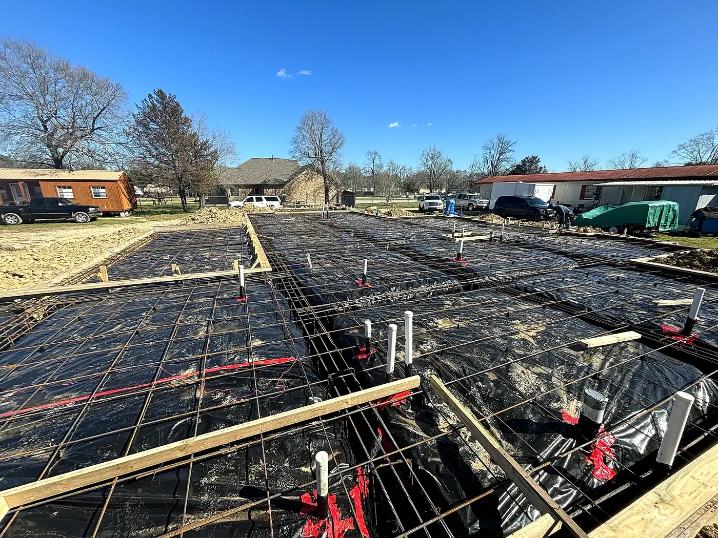 Slab foundation before the pour: vapor barrier, rebar grid on chairs, and beam trenches