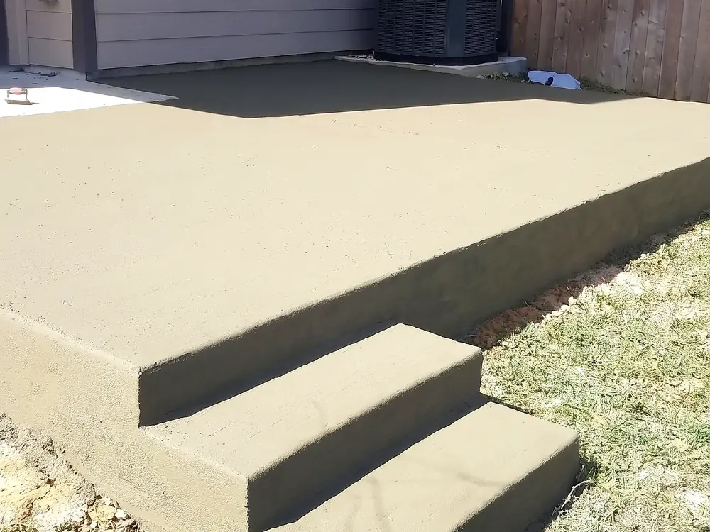 Freshly poured backyard concrete patio with integrated corner steps, still curing
