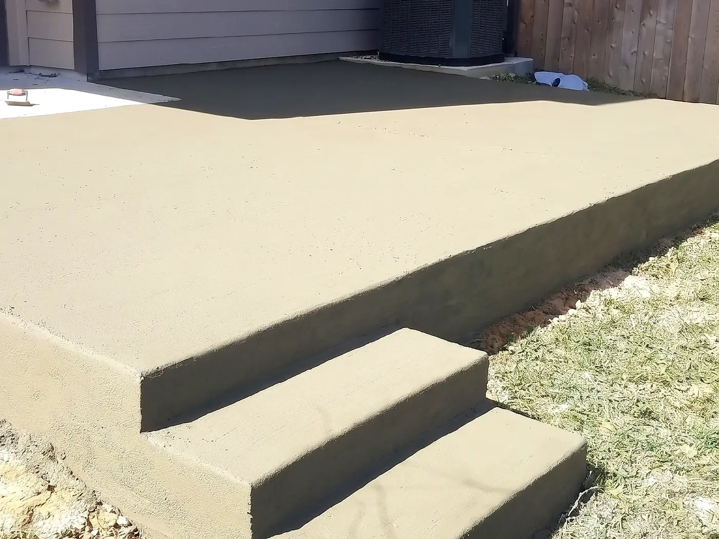 Freshly poured backyard concrete patio with integrated corner steps, still curing
