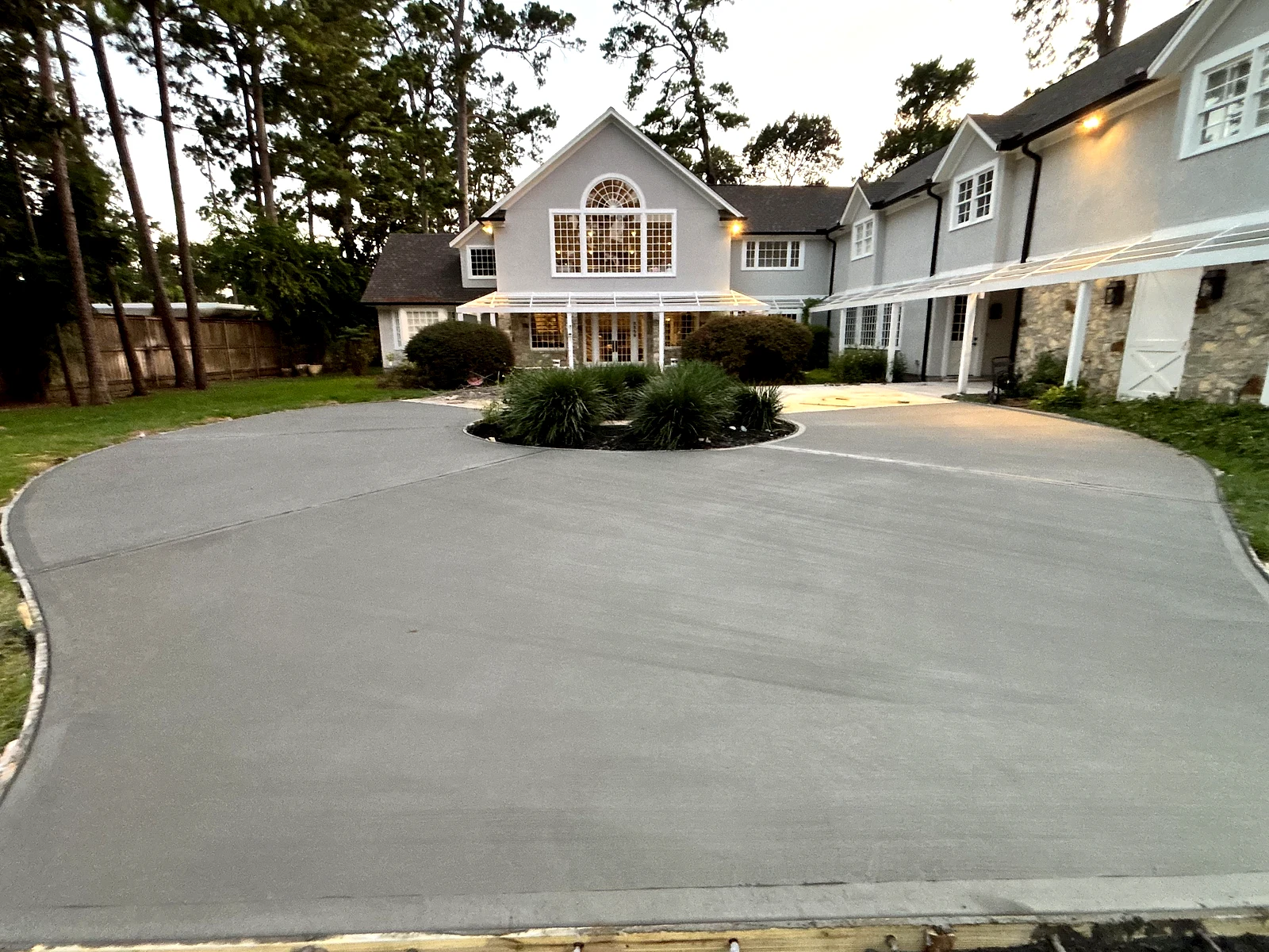 The same property with its finished concrete driveway sweeping around a planted island at dusk