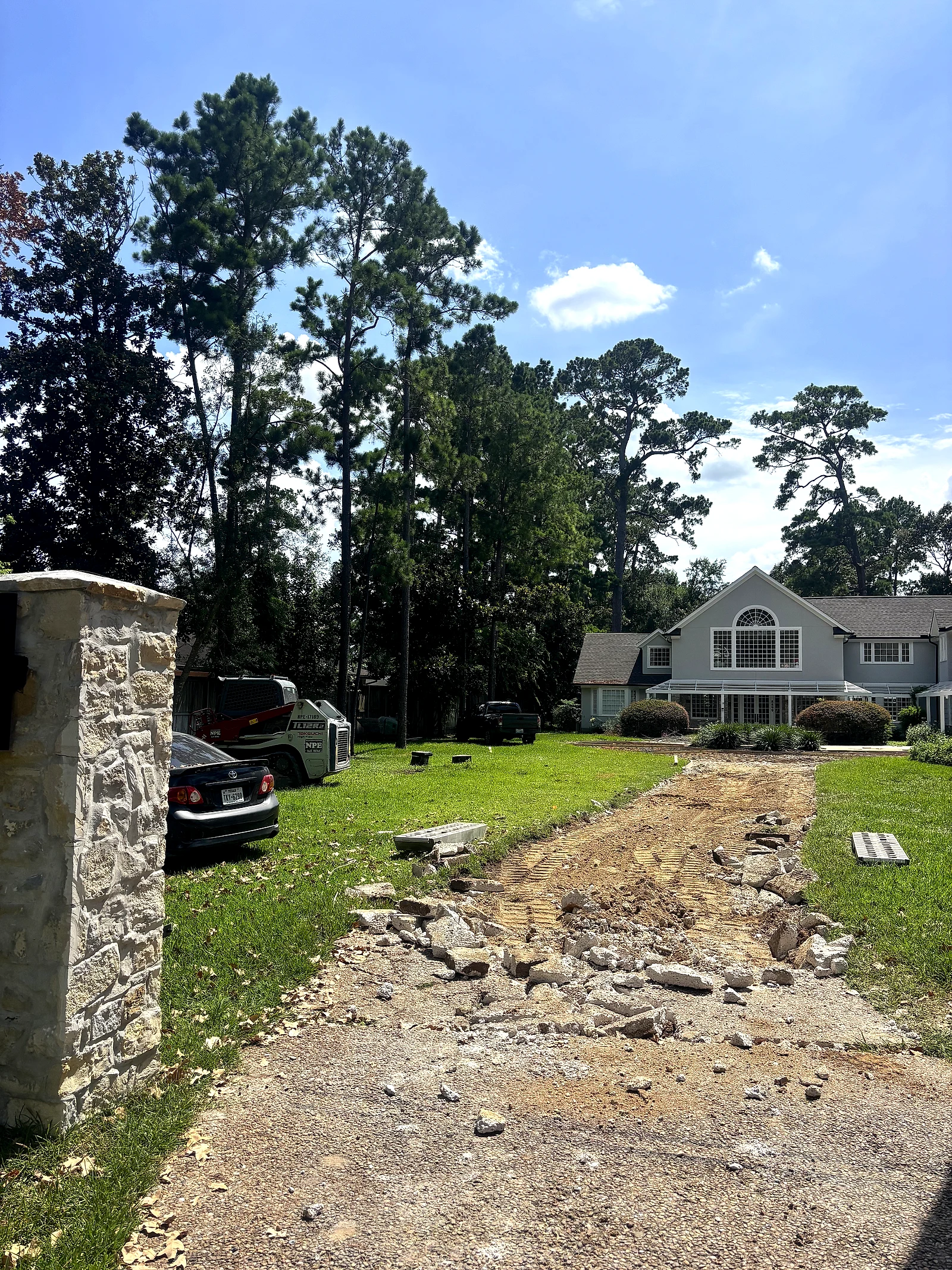 Old driveway demolished to rubble and dirt in front of a two-story home, before base preparation