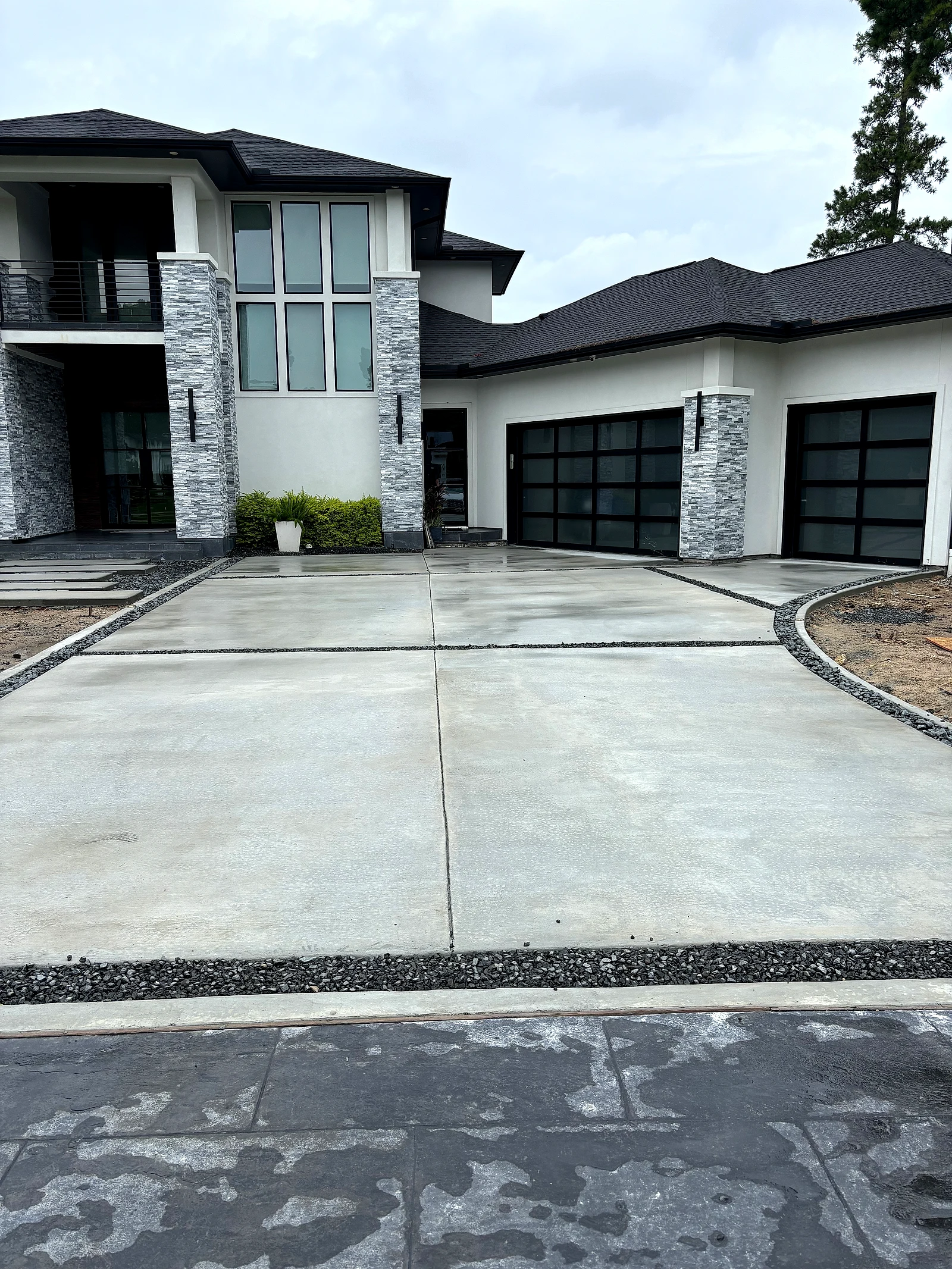Fresh gray concrete driveway with dark rock borders at a modern new-construction home