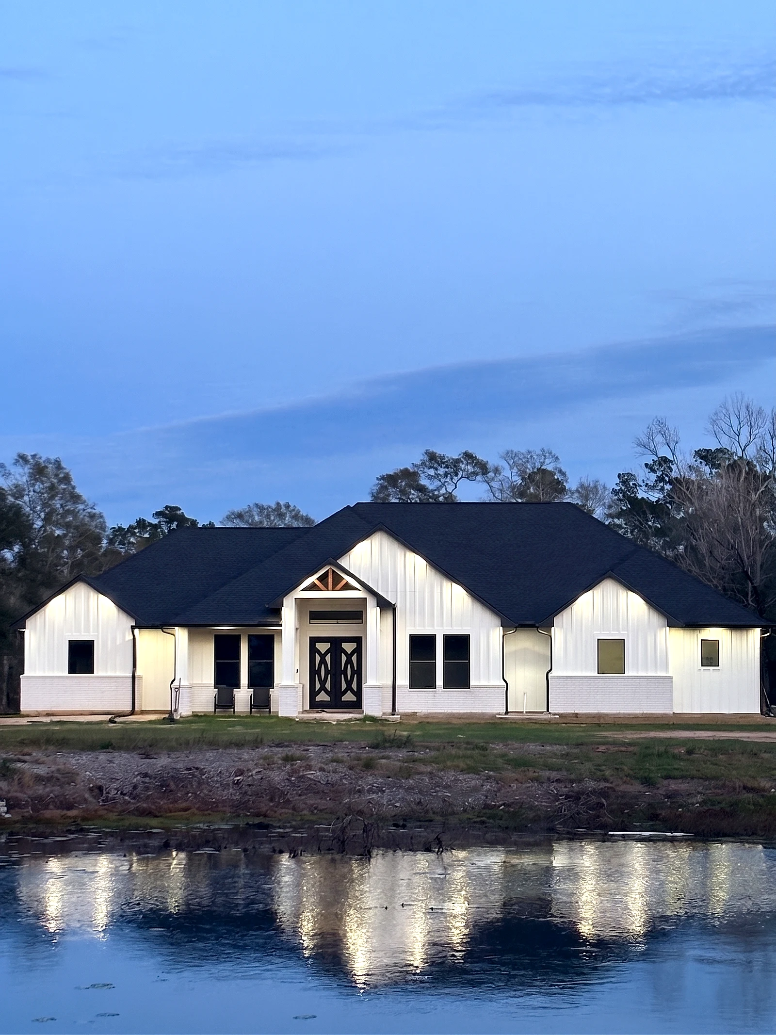 Completed custom home at dusk, lights on, reflected in a pond