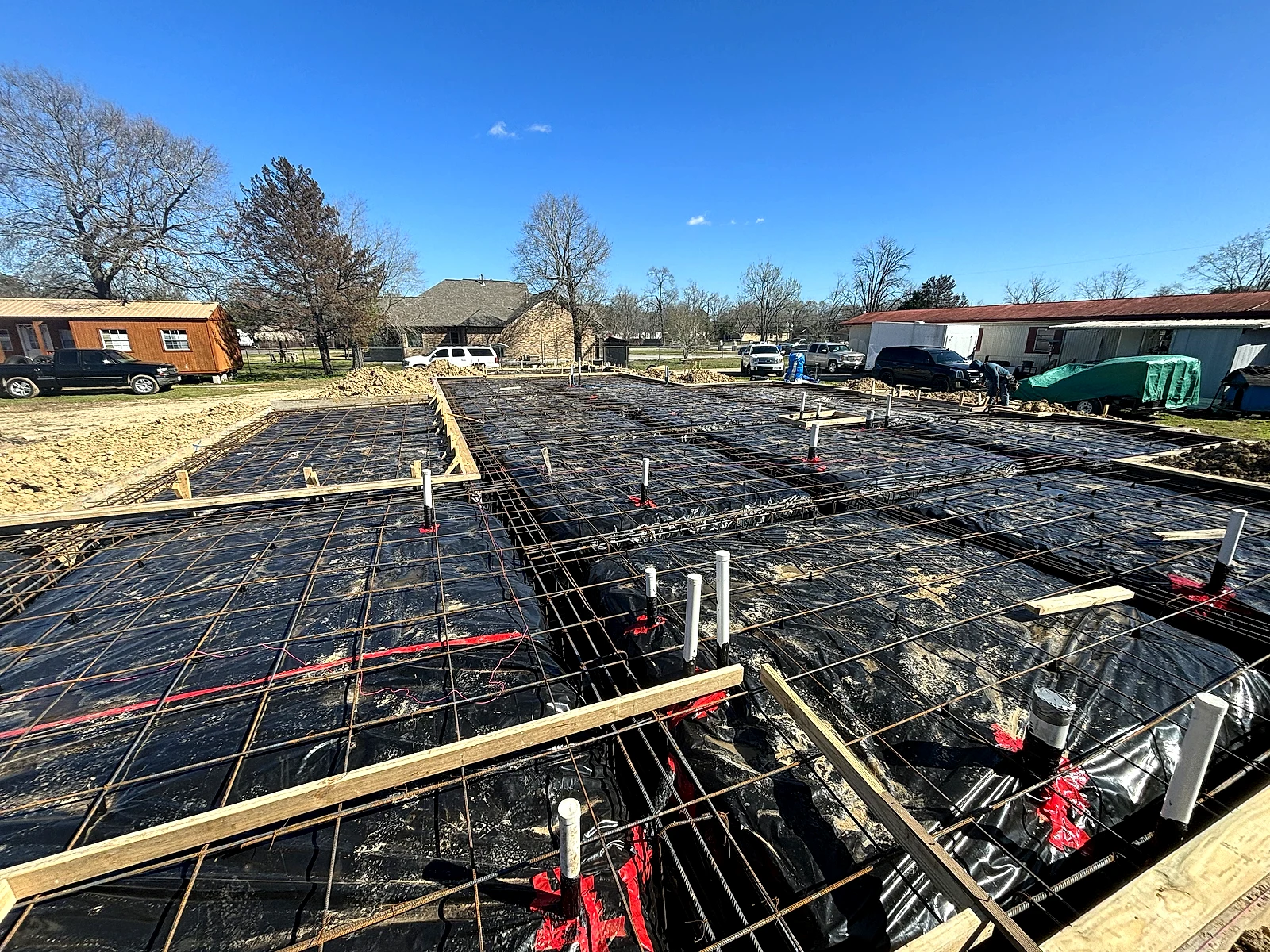 Slab foundation before the pour: vapor barrier, rebar grid on chairs, and beam trenches