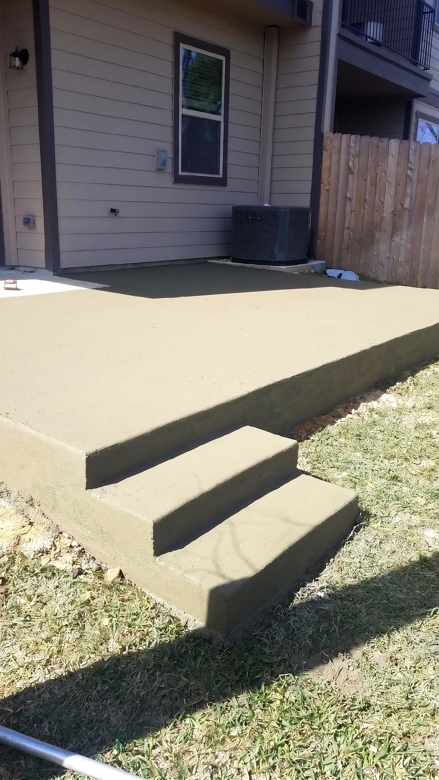 Freshly poured backyard concrete patio with integrated corner steps, still curing